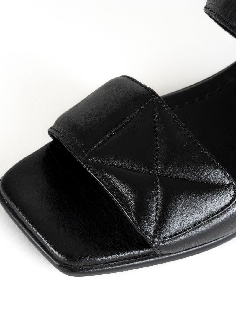 Detailfoto einer minimalistischen Sandale in schwarzem Glattleder mit Karree Leisten und zwei gepolsterten Riemen mit dekorativen Nähten im Quilted-Look