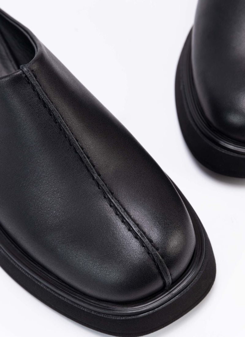 Nahaufnahme der Schuhfront eines coolen Clog-Modells aus schwarzem, zertifiziertem Echtleder. Gut zu sehen ist das Design-Detail, eine raffinierte Wulstnaht, die den Schuhschaft optisch in zwei Seiten unterteilt.