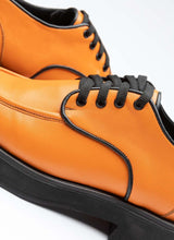 Load image into Gallery viewer, Detailansicht eines orangefarbenen Unisex-Lederschuhs mit Schnürsenkeln in schwarz, farblich angesetzter Paspel in schwarz und einer dezenten, schwarzen Plateausohle