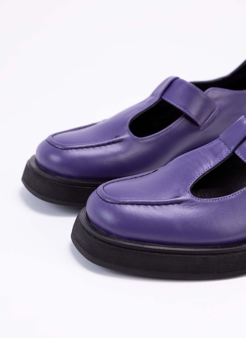 Detailaufnahme eines lilafarbenen Lederschuhs. Zu sehen ist die Schuhspitze mit der schwarzen Wulstnaht. Außerdem sind die Aussparungen auf dem Fußrücken zu erkennen, die das Modell zu einem typischen Mary Jane Shoe machen.