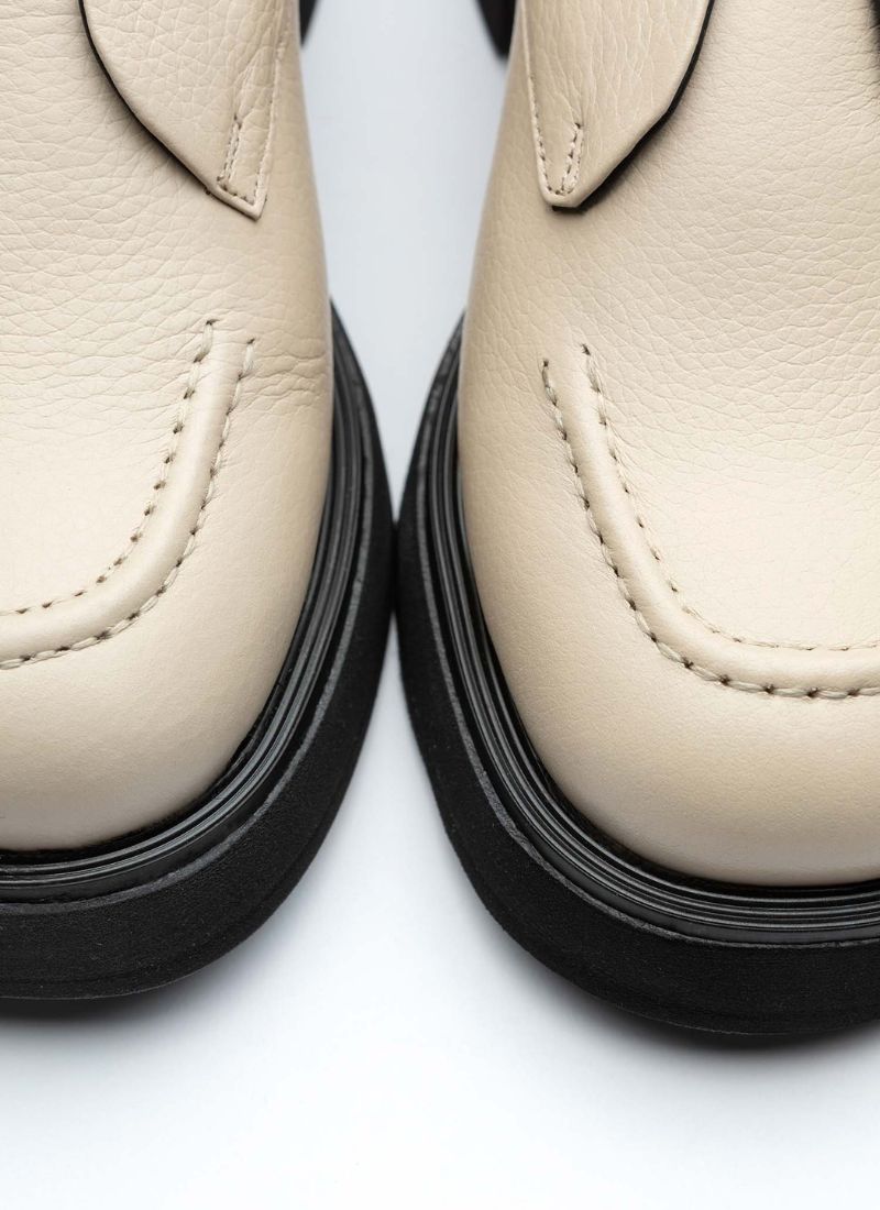 Schuhspitze eines cremefarbenen Halbschuhs aus Leder mit dezent genarbter Oberfläche. Gut zu erkennen ist die Wulstnaht mit farblich passendem Stitching. Die Laufsohle ist schwarz und verfügt über ein leichtes Plateau.