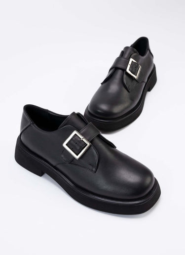 Ein Paar luxuriöse Halbschuhe aus hochwertigem, schwarzem Leder mit Lederriemen über dem Spann und silberfarbener, eckiger Schnalle. Auch die Sohle und das Futter sind passend schwarz. Die Schuhe sind vom Hersteller Cedoublé und werden unter fairen Bedingungen in Europa produziert.