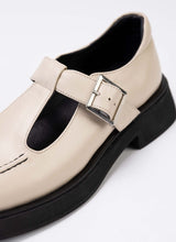 Lade das Bild in den Galerie-Viewer, Detailaufnahme eines Mary Jane Schuhs aus cremefarbenem Leder mit dezentem Perlglanz. Das Modell verfügt über einen T-Steg, eine silberfarbene Schnalle, eine schwarze Laufsohle und schwarzes Lederfutter.