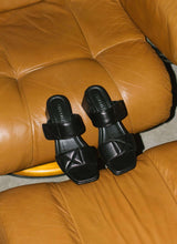 Load image into Gallery viewer, Elegant-alltagstaugliche Absatzsandale aus schwarzem Leder mit Karreefront auf einem cognacfarbenen Ledersessel