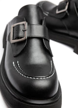 Load image into Gallery viewer, Schuhspitze eines schwarzen, modischen Leder-Clogs. Zu sehen sind die abgerundete Karree-Form und ein Teil der leichten EVA-Sohle. Über dem Spann verläuft eine Monk-Schnalle in der Farbe Silber. Modisches Highlight ist zudem die weiße Naht, die auf der Schuhspitze verläuft.