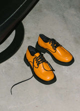 Load image into Gallery viewer, Ein Paar orangefarbener unisex Lederschnürer steht auf einem Betonboden und wird von einem harten Licht angestrahlt