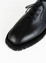 Load image into Gallery viewer, Detailfoto eines burschikosen Leder Derbys mit Oxford-Schnürung und ausgeprägter Laufsohle in schwarz. Eine asymmetrische Naht ziert die Schuhfront