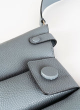 Load image into Gallery viewer, Detailfoto einer Crossbody-Bag aus grauem, genarbtem Leder mit drei voneinander abgetrennten Fächern und einem farblich passenden, breiten Gurt aus Leder mit Karabinerhaken. Diese Handtasche ist genderfluid, angefertigt wurde sie von dem Newcomer-Label Cedoublé.