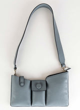 Load image into Gallery viewer, Produktfoto einer grauen Crossbody Tasche, deren Kalbsleder in einem hellen Kieselgrau gehalten ist. Die Oberfläche weist eine dezent körnige Narbung auf, aus diesem Grund trägt die Handtasche unter anderem den Beinamen "pebbled". Weiterhin wird sie von den Gründerinnen der Marke auch als Toolbag bezeichnet, da es sich um ein praktisches Format handelt und in den drei Fächern alles Notwendige untergebracht werden kann. Die Marke ist CEDOUBLÉ.