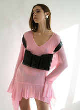 Load image into Gallery viewer, Foto eines weiblichen Models mit langen braunen Haaren. Sie trägt ein leicht transparentes, hell pinkfarbenes Kleid mit gezackten Säumen, eine schwarze Handtasche aus Leder ist künstlerisch um beide Schultern gehängt, der Taschenkörper zeigt nach vorne und baumelt etwa auf Unterbrusthöhe der Frau. Das Model hat ihren Blick zur Seite gerichtet, sie steht vor einem weißen Hintergrund. Die Tasche ist von der Marke Cedoublé.