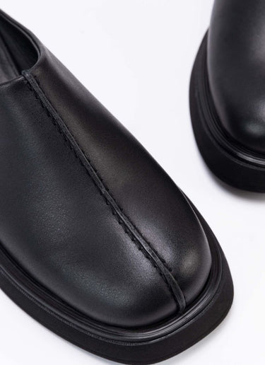 Nahaufnahme der Schuhfront eines coolen Clog-Modells aus schwarzem, zertifiziertem Echtleder. Gut zu sehen ist das Design-Detail, eine raffinierte Wulstnaht, die den Schuhschaft optisch in zwei Seiten unterteilt. 