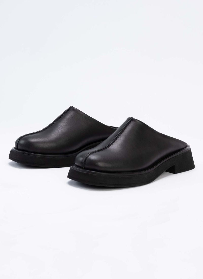 Seitliche Ansicht eines Paares Unisex-Clogs aus traumhaftem Echtleder in zeitlosem Schwarz. Die Schuhe sind mit Modellen von Vagabond vergleichbar. Durch die breite Größenauswahl ist das Modell von Frauen und Männern tragbar. Das Label Cedoublé fertigt ausschließlich in Europa und legt einen Fokus auf nachhaltiges Verhalten in allen Belangen.