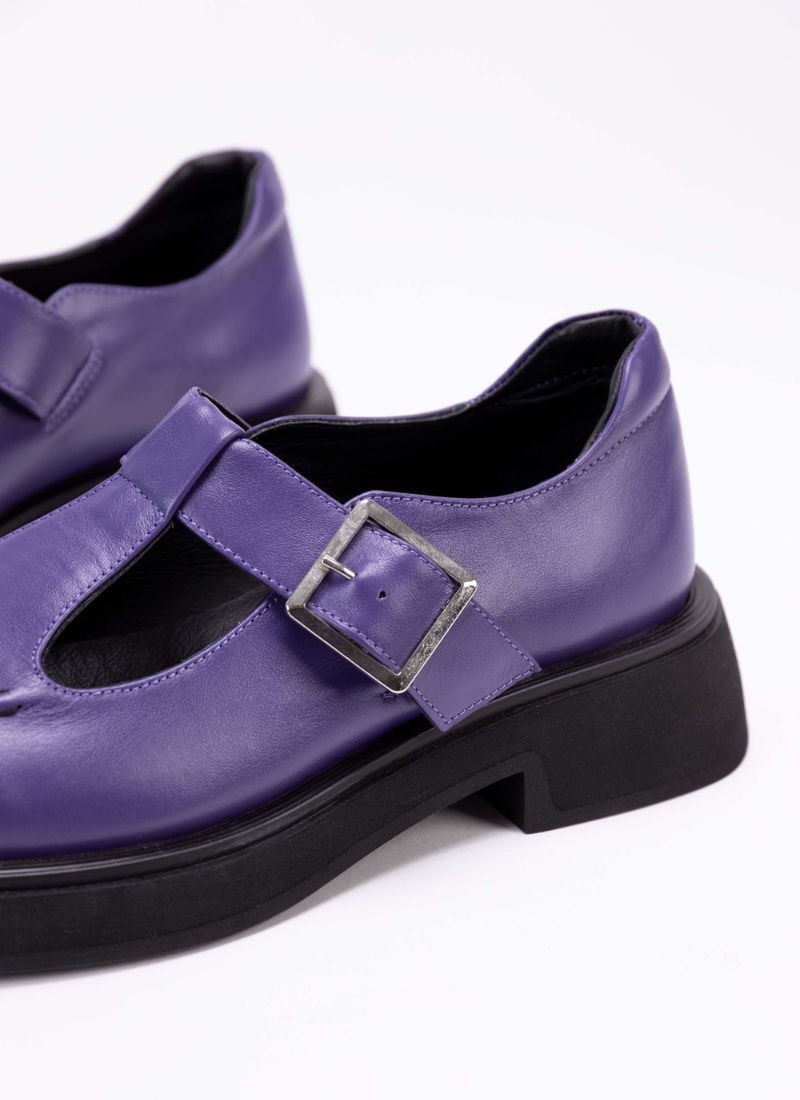 Detailaufnahme eines Lederschuhs in der Farbe lila. Das Modell nennt sich Mary Jane und verfügt über die für diesen Schuhtyp charakteristischen Details wie den T-Steg und die Aussparungen auf dem Fußrücken. Die Laufsohle ist schwarz. Das Lederfutter ist ebenfalls schwarz.