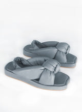 Load image into Gallery viewer, Produktbild einer weich gepolsterten Sandale aus grauem Leder mit exzentrischem Knotdendetail, welches den Fuß umhüllt. Ein weicher, geraffter Lederriemen in blau-grau fixiert die Ferse. Die Deck- und Laufsohle sind mit grauem Leder bezogen  
