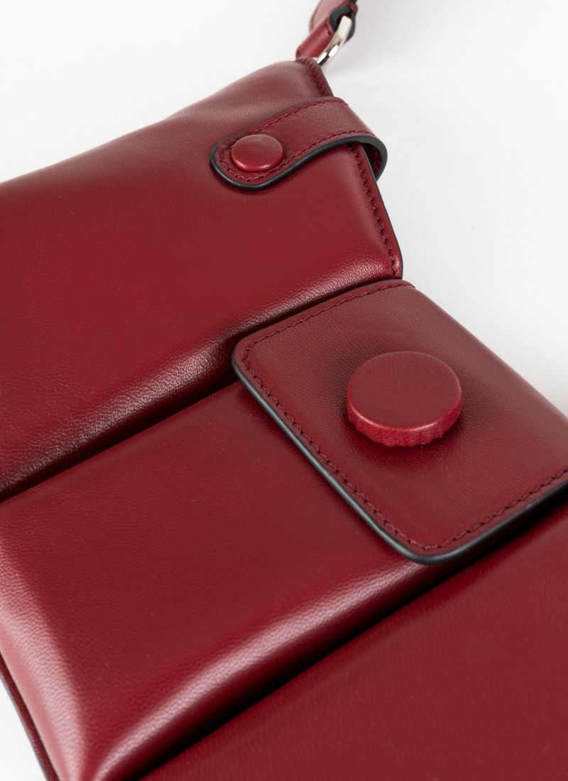 Detailfoto einer dunkelroten Crossbody-Bag aus weich gepolstertem Glattleder mit drei voneinander abgetrennten Fächern und einem farblich passenden, breiten Gurt aus Leder mit Karabinerhaken