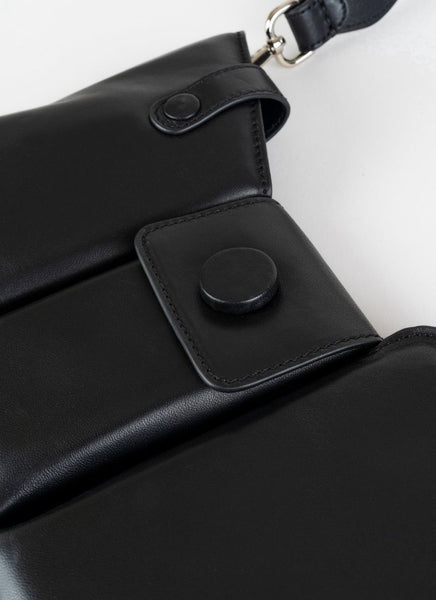 Detailfoto einer schwarzen Crossbody-Bag aus weich gepolstertem Glattleder mit drei voneinander abgetrennten Fächern und einem farblich passenden, breiten Gurt aus Leder mit Karabinerhaken