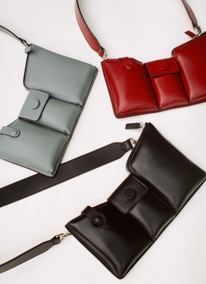 Three leather bags on a white background. Two are made out of puffy leather – one in dark red and one in black – and the third one is made out of grey, pebbled leather.