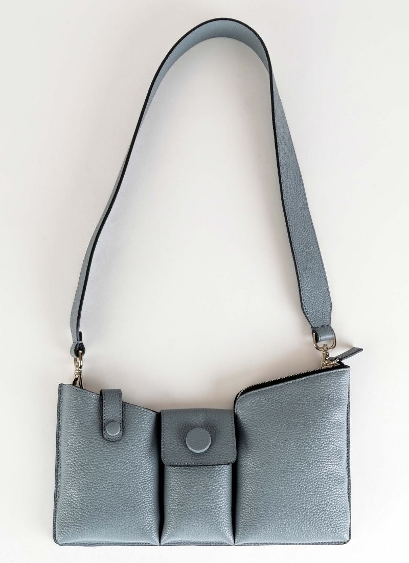 Produktfoto einer grauen Crossbody Tasche, deren Kalbsleder in einem hellen Kieselgrau gehalten ist. Die Oberfläche weist eine dezent körnige Narbung auf, aus diesem Grund trägt die Handtasche unter anderem den Beinamen "pebbled". Weiterhin wird sie von den Gründerinnen der Marke auch als Toolbag bezeichnet, da es sich um ein praktisches Format handelt und in den drei Fächern alles Notwendige untergebracht werden kann. Die Marke ist CEDOUBLÉ.