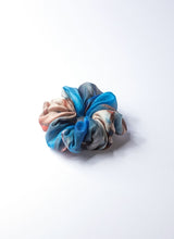 Load image into Gallery viewer, Elastisches Haargummi aus 100% upcycled Seide, welche von einem hochwertigen Seidentuch im Batiklook stammt. Das Scrunchie weist einen Farbverlauf auf, bei den Tönen handelt es sich um türkisblau, sandfarben und terracotta.
